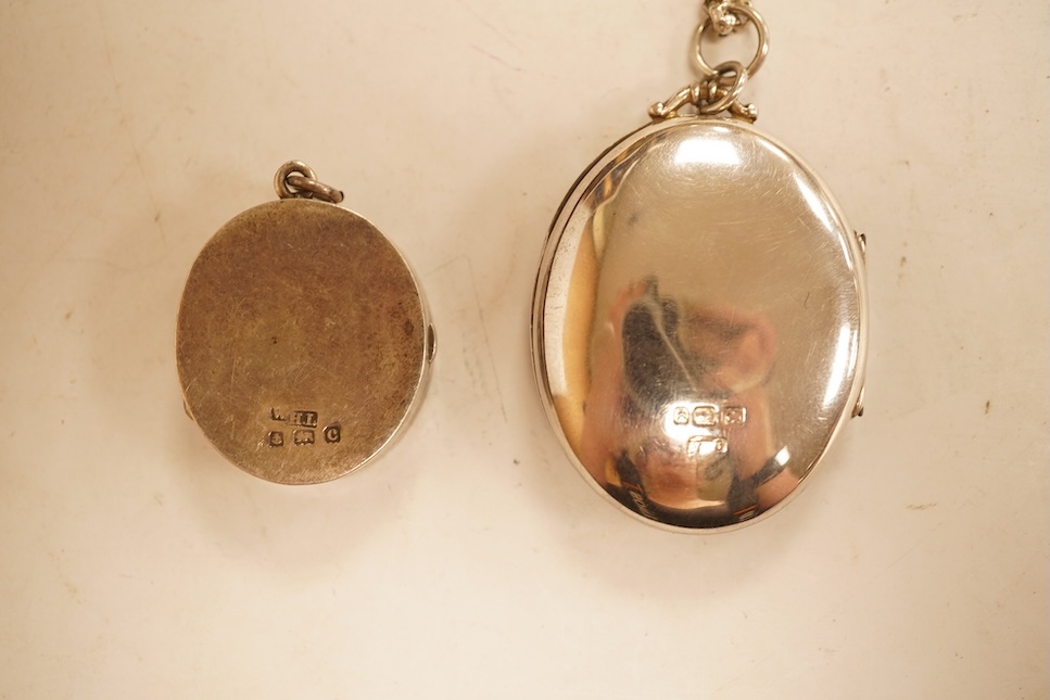 A late Victorian embossed and engraved oval silver locket, 42mm, on a later white meta belcher link chain, together with an Edwardian silver and hardstone inlaid pill box, now with pendant mount.